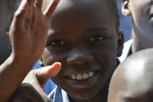 Ein afrikanicher Junge winkt lächelnd in die Kamera