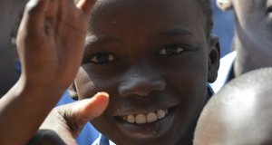 Ein afrikanicher Junge winkt lächelnd in die Kamera