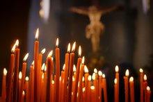 Brennende Kerzen in einem Kirchenraum, im Hintergrund das Kreuz