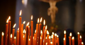 Brennende Kerzen in einem Kirchenraum, im Hintergrund das Kreuz