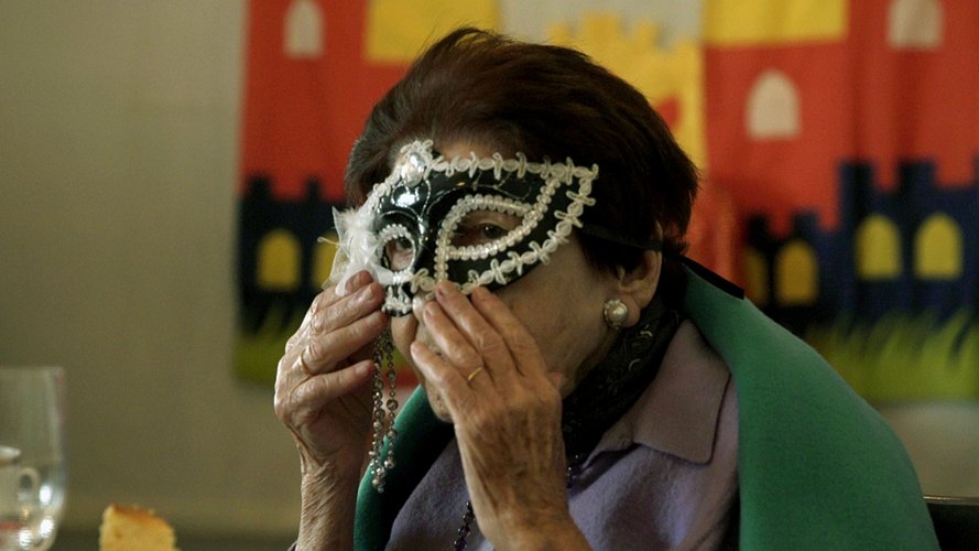 Seniorin hält sich venizianische Karnevalsmaske vor das Gesicht